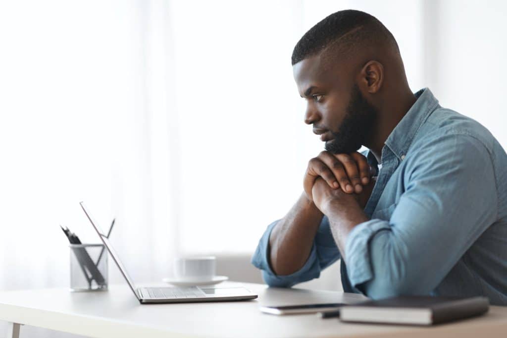 Thoughtful Black Writer Working With Laptop Computer At Home Office, Side View